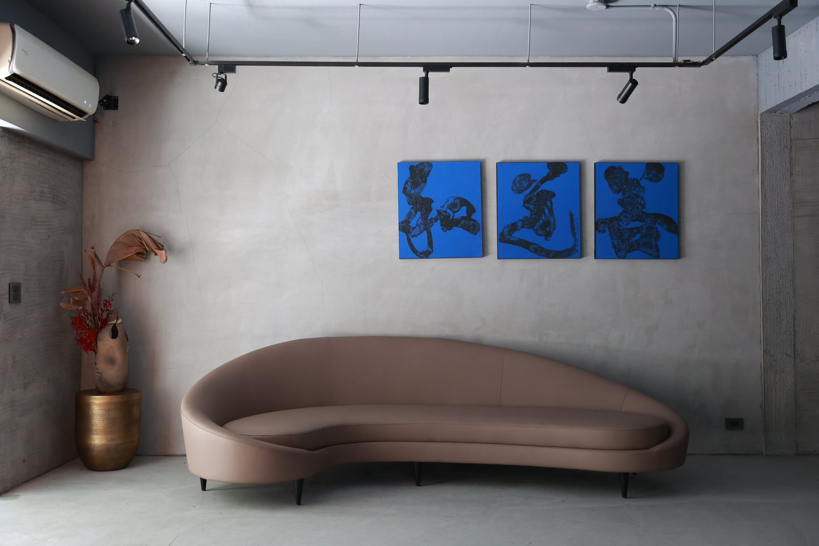 Three blue-ground calligraphies above a curved velvet sofa in a concrete room