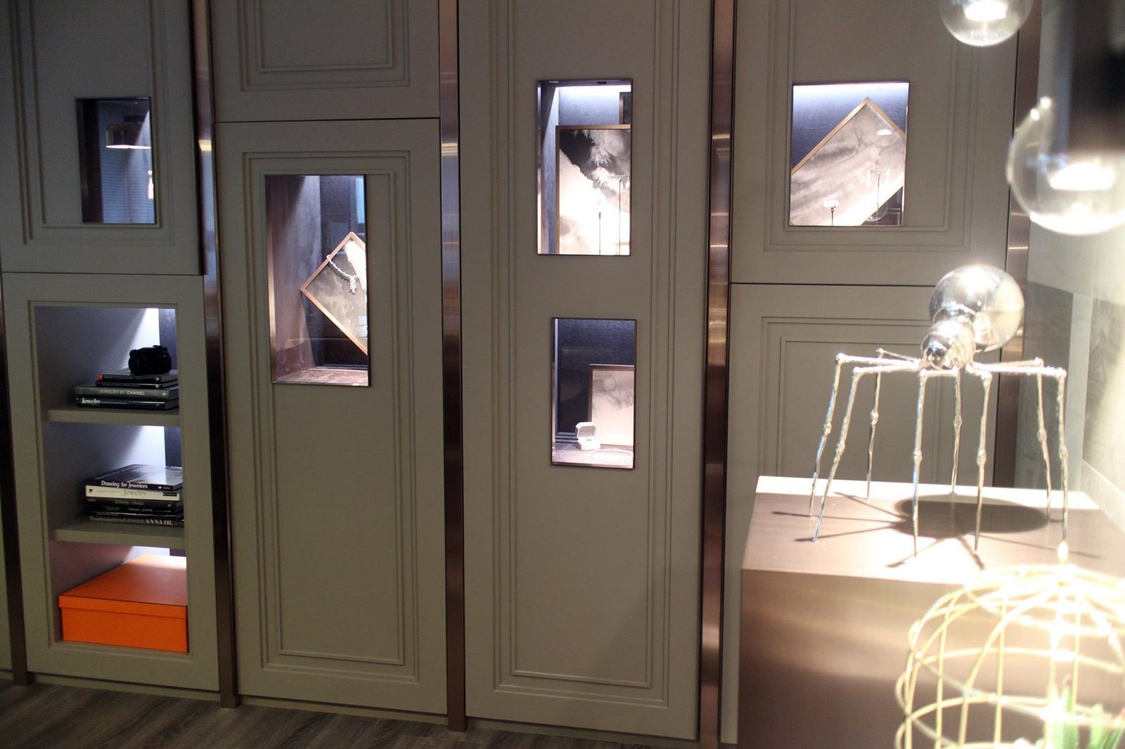 Ink-wash panels in bronze frames behind jewellery in the lit display niches of a Taipei jeweller
