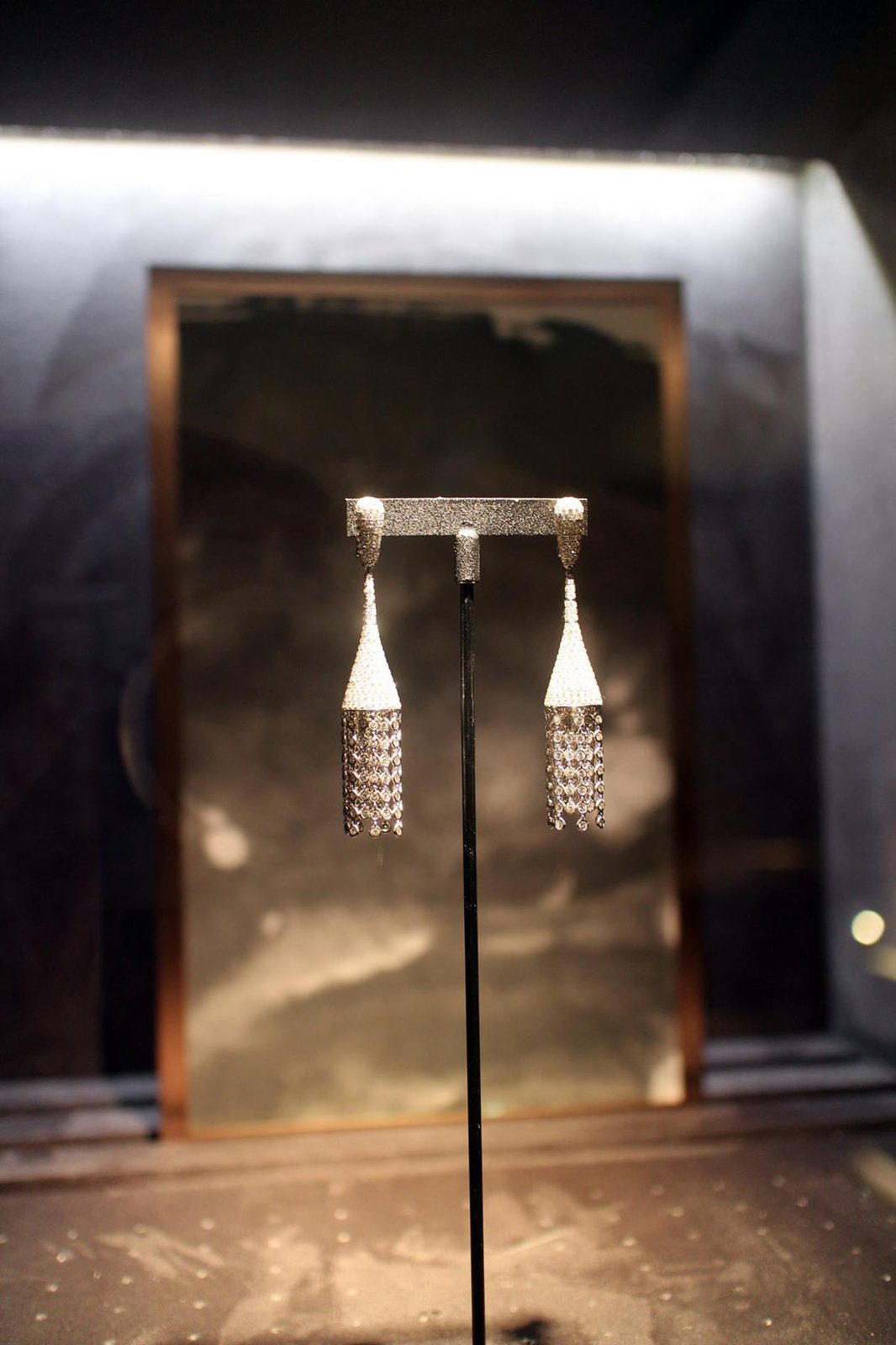 Ink-wash panels in bronze frames behind jewellery in the lit display niches of a Taipei jeweller