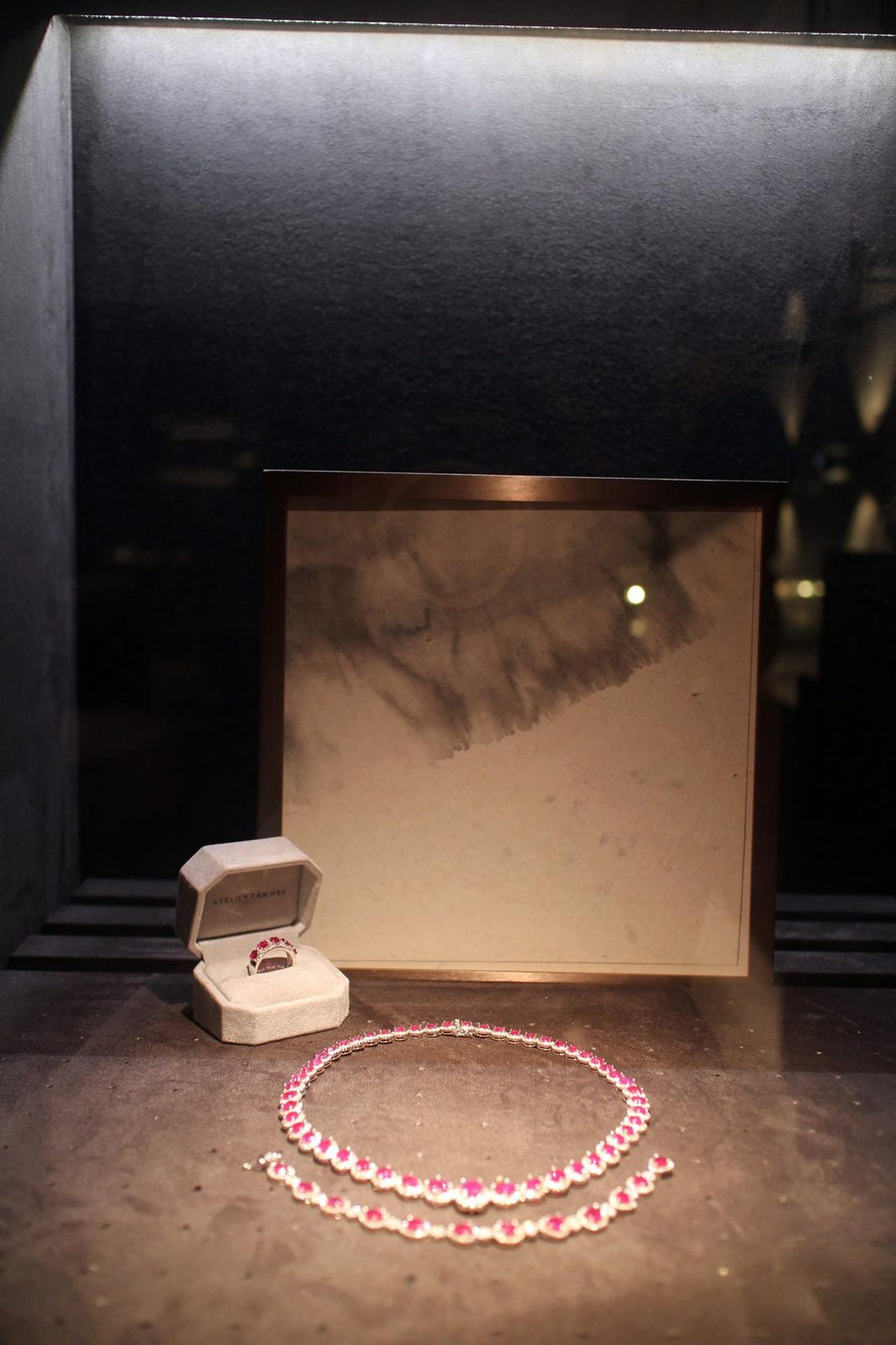 Ink-wash panels in bronze frames behind jewellery in the lit display niches of a Taipei jeweller