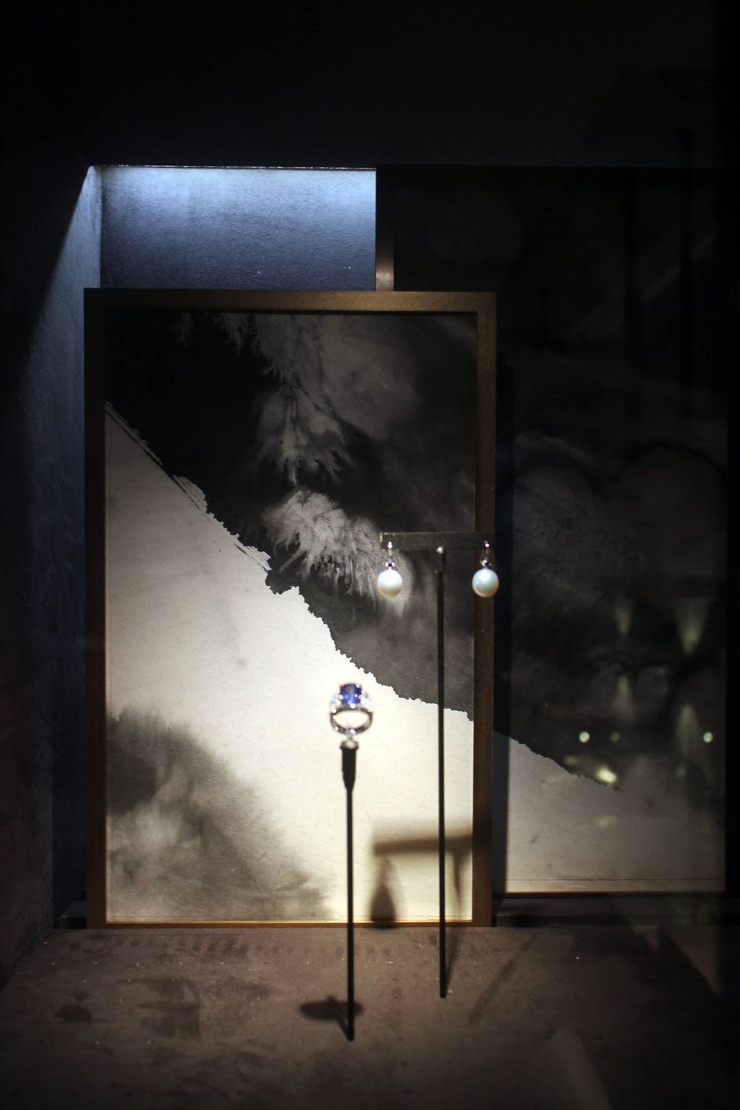 Ink-wash panels in bronze frames behind jewellery in the lit display niches of a Taipei jeweller