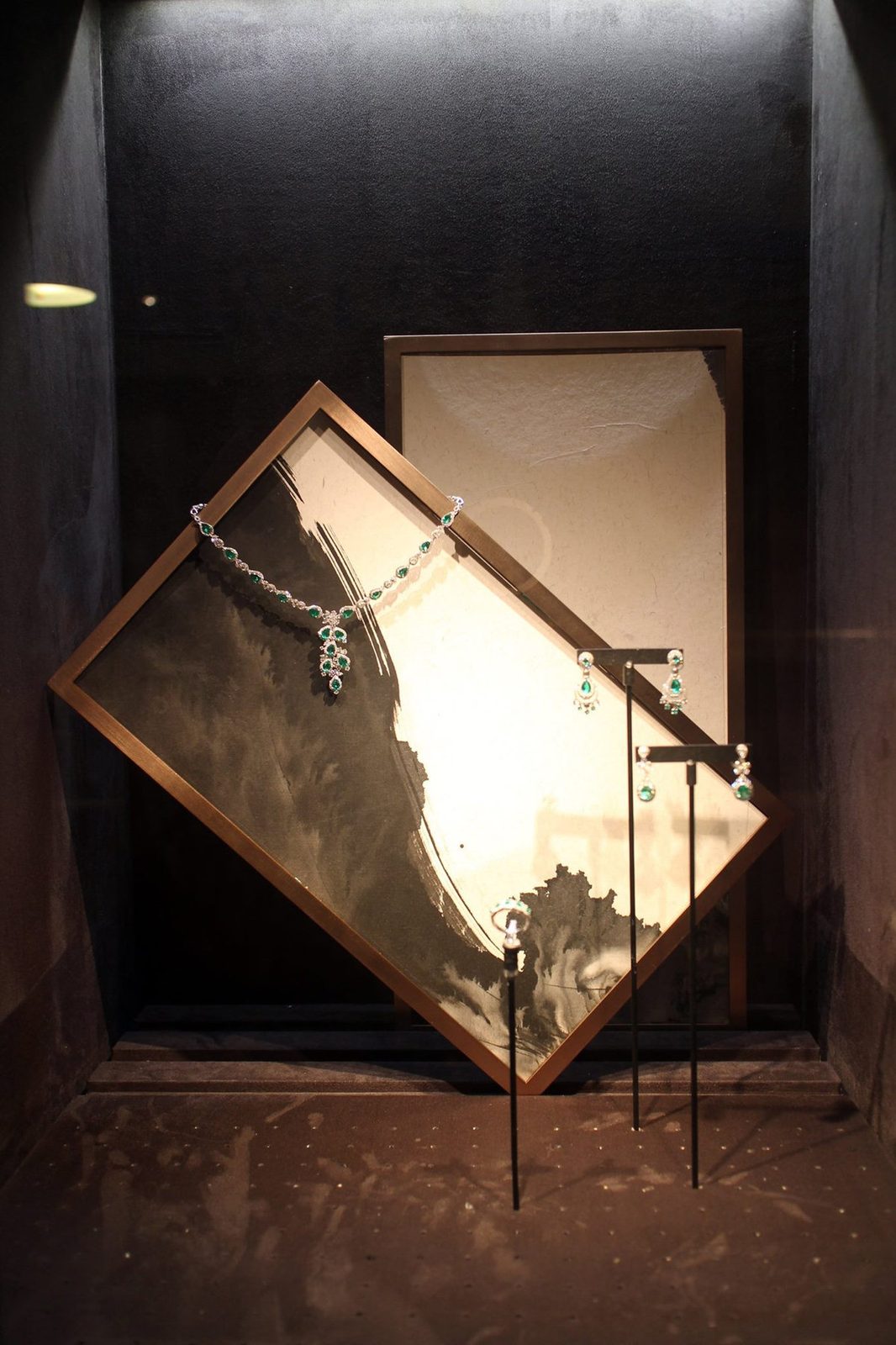 Ink-wash panels in bronze frames behind jewellery in the lit display niches of a Taipei jeweller
