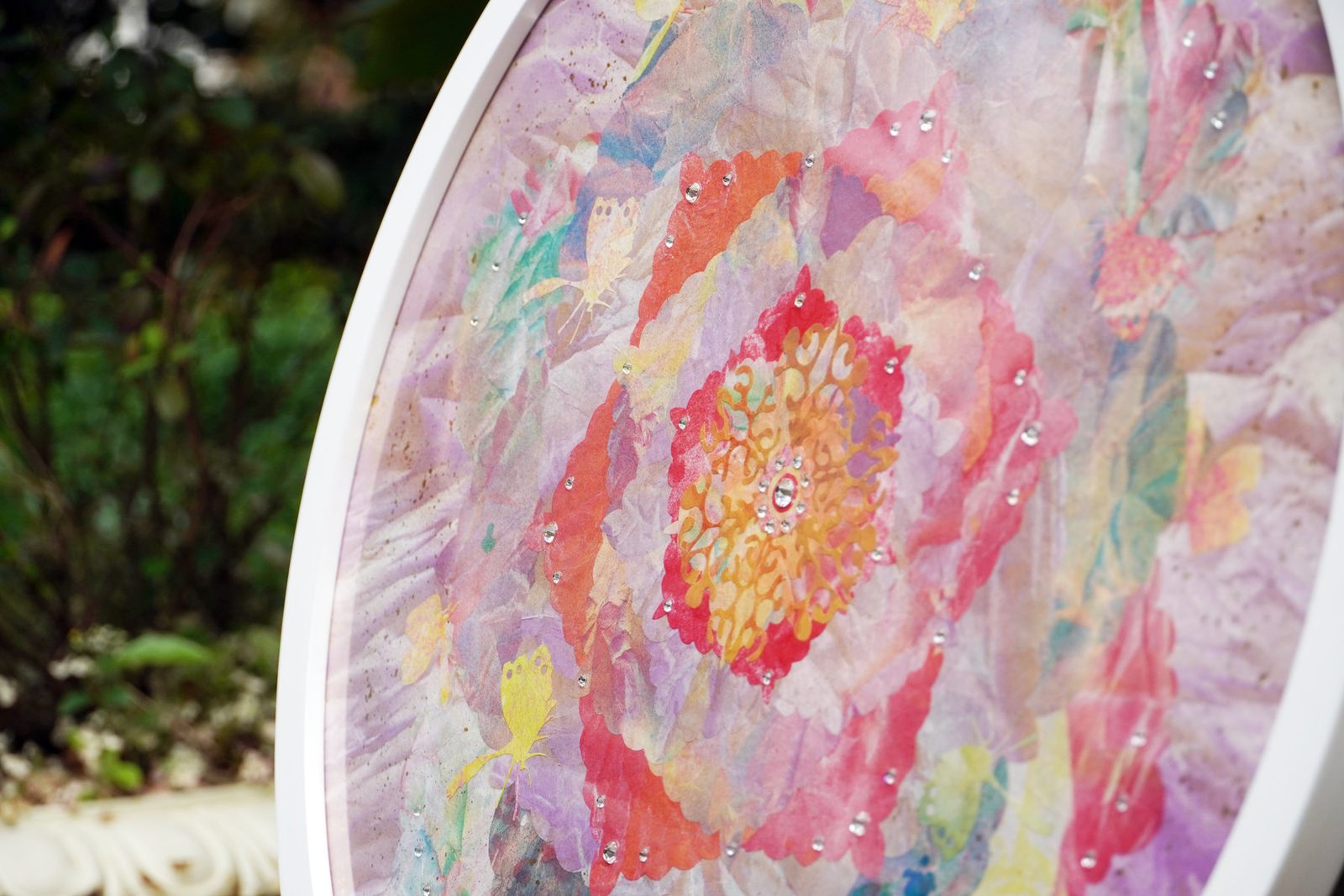 A round mineral painting in pink and coral on an easel among spring greenery at an evening exhibition