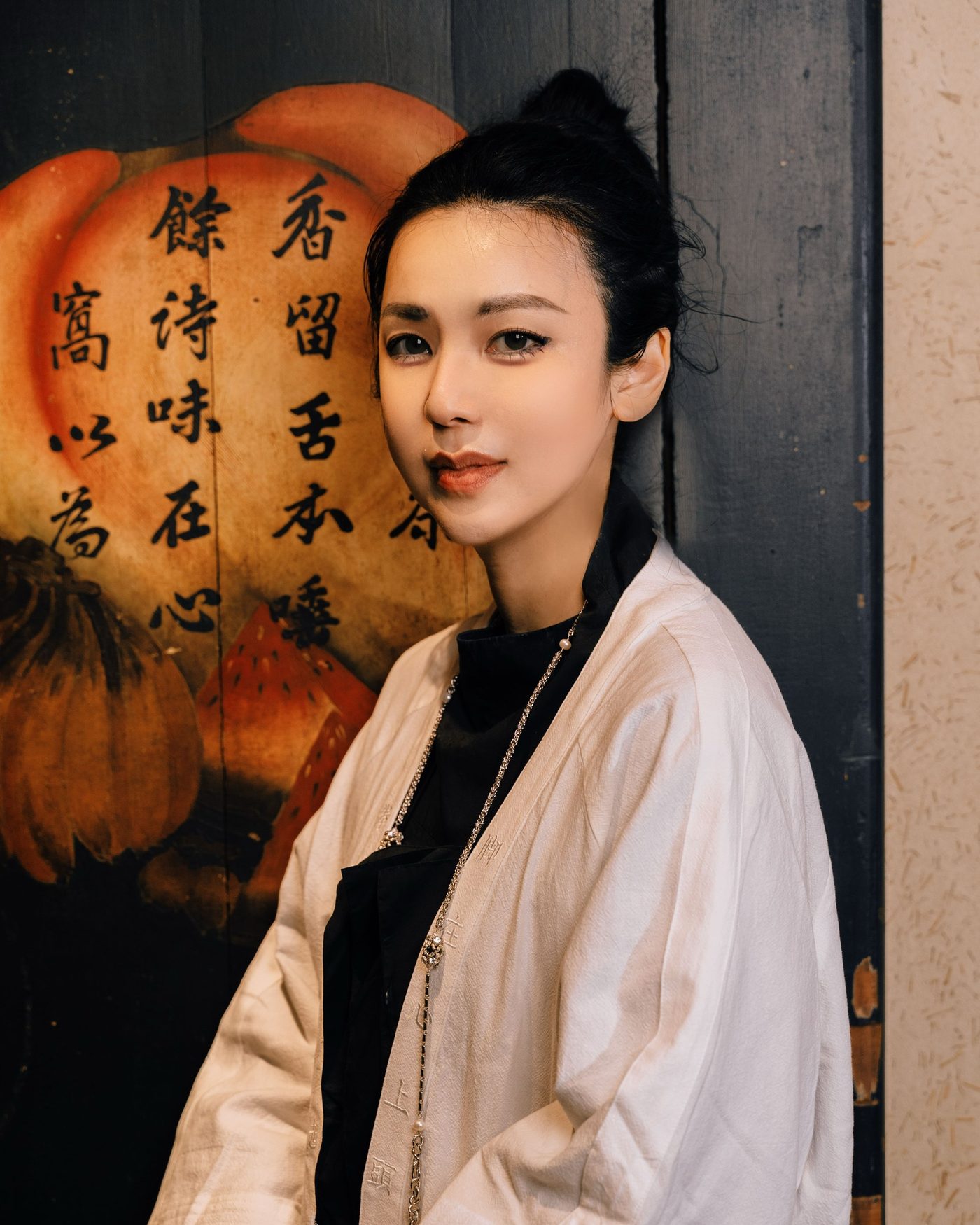 Ku Chi-Chun in a cream linen jacket over black, before a dark lacquered panel lettered in calligraphy