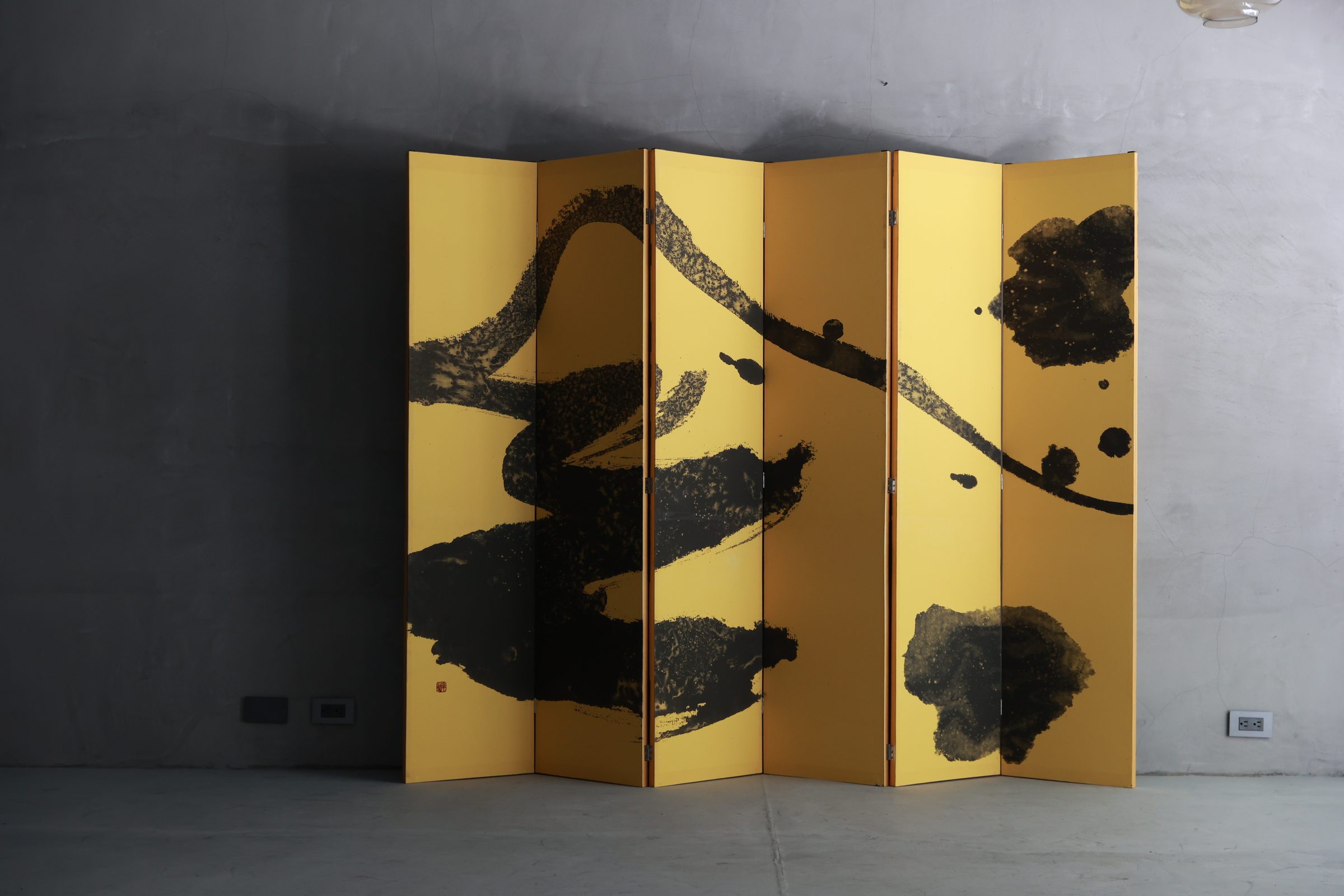 Ku Chi-Chun's six-panel gold folding screen, painted in black ink, standing whole against a concrete wall