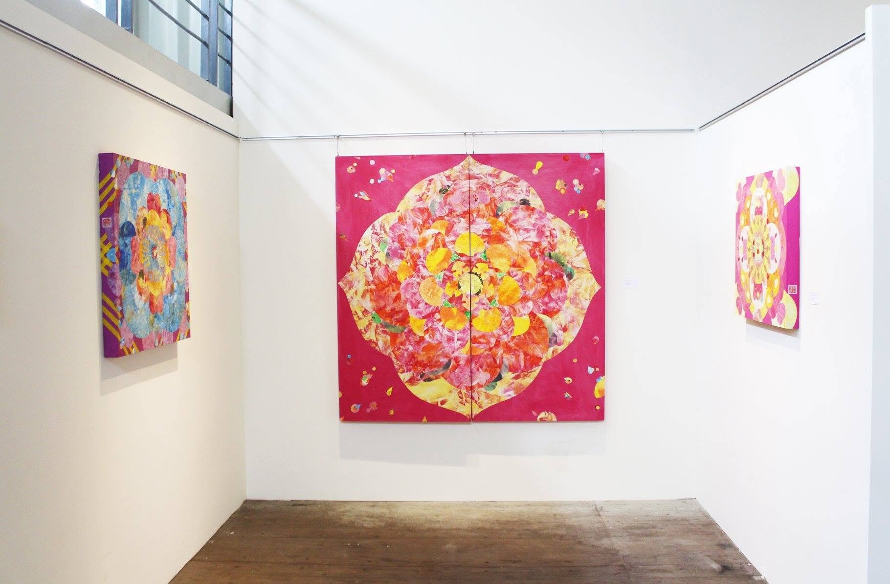 A large red mineral painting in a mandala form on a white gallery wall, two smaller works in the same palette on the side walls