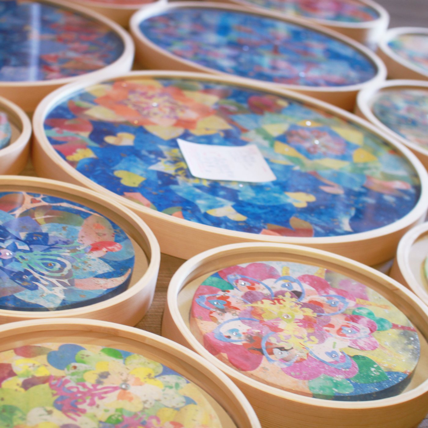 Round mineral paintings in pale wooden frames laid out on a table, mandalas in blue, coral, pink and gold