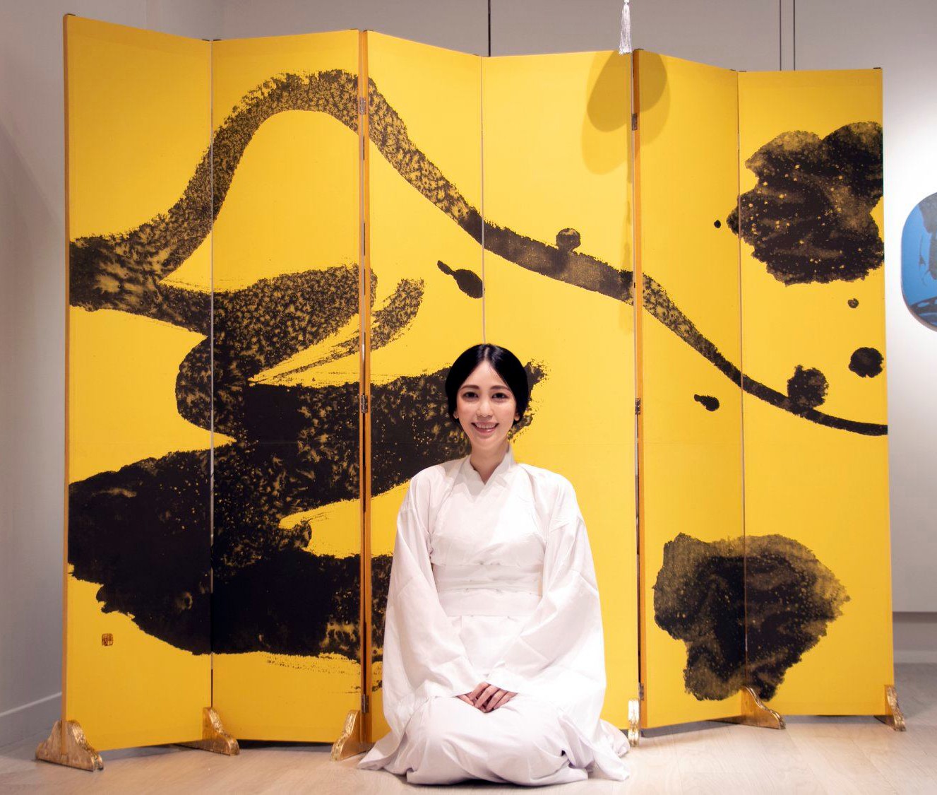 Ku Chi-Chun, smiling, seated in white before her gold six-panel screen painted in black ink