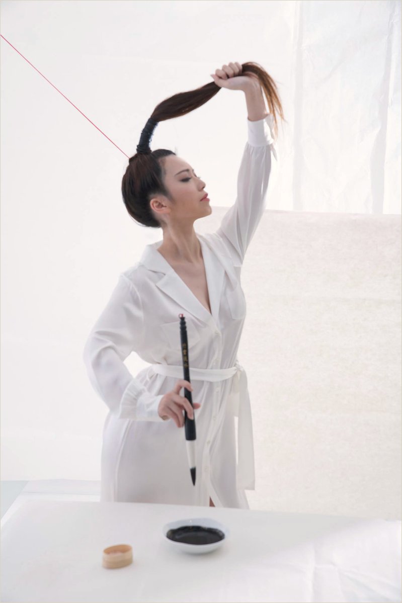 Ku Chi-Chun in a white robe in the Taipei studio, a brush in her hand and a dish of ink on the table