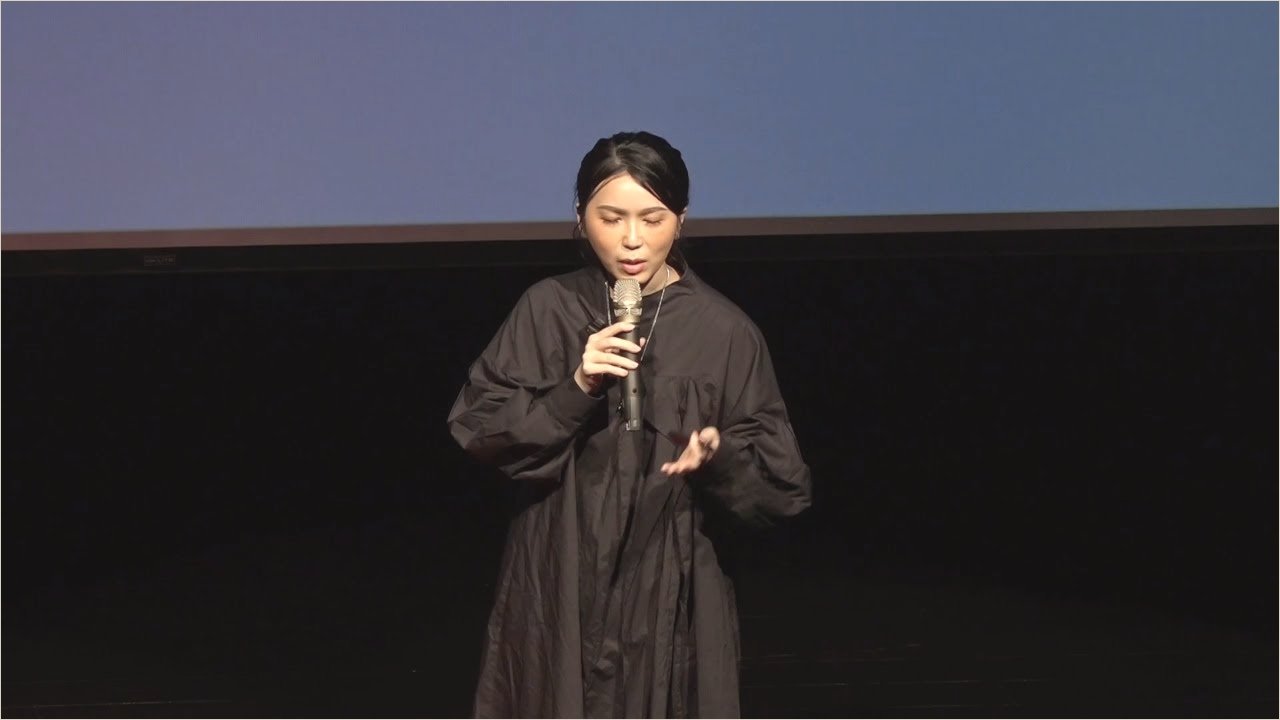 Ku Chi-Chun on the TEDxYongkang stage in the official TEDx Talks recording, the auditorium dark around her
