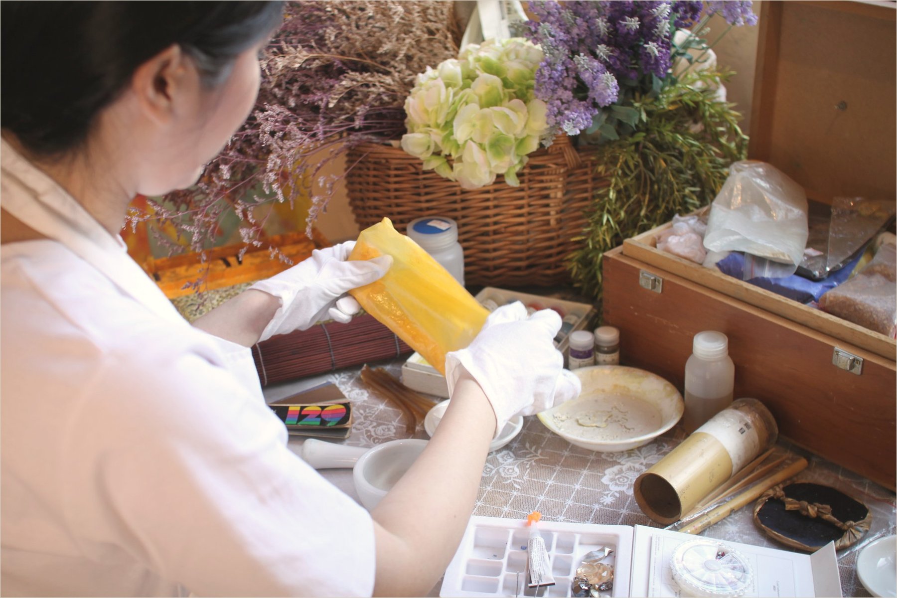 Gloved hands tearing a sheet of gold leaf beside the pigment box