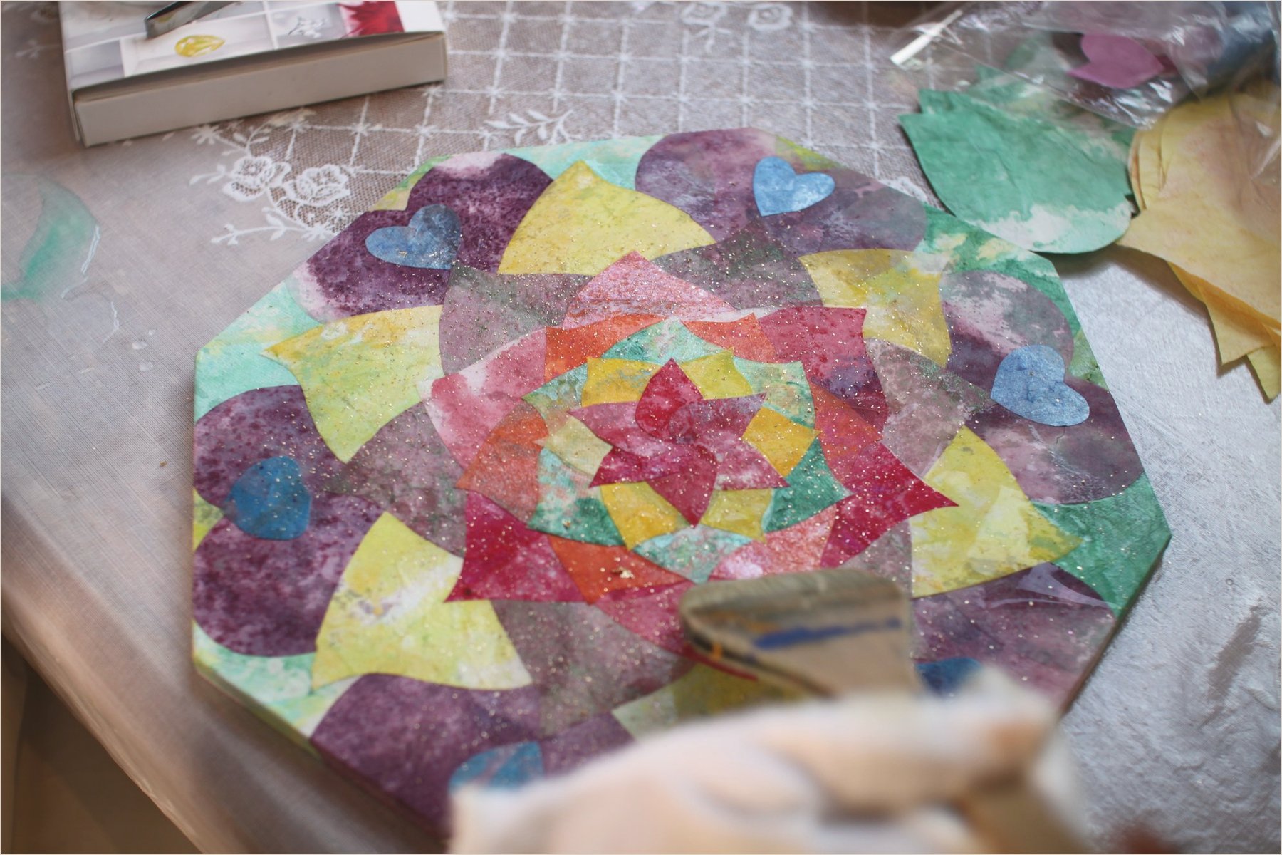 A brush laying colour on the octagonal mandala board, its crinkled paper petals half covered