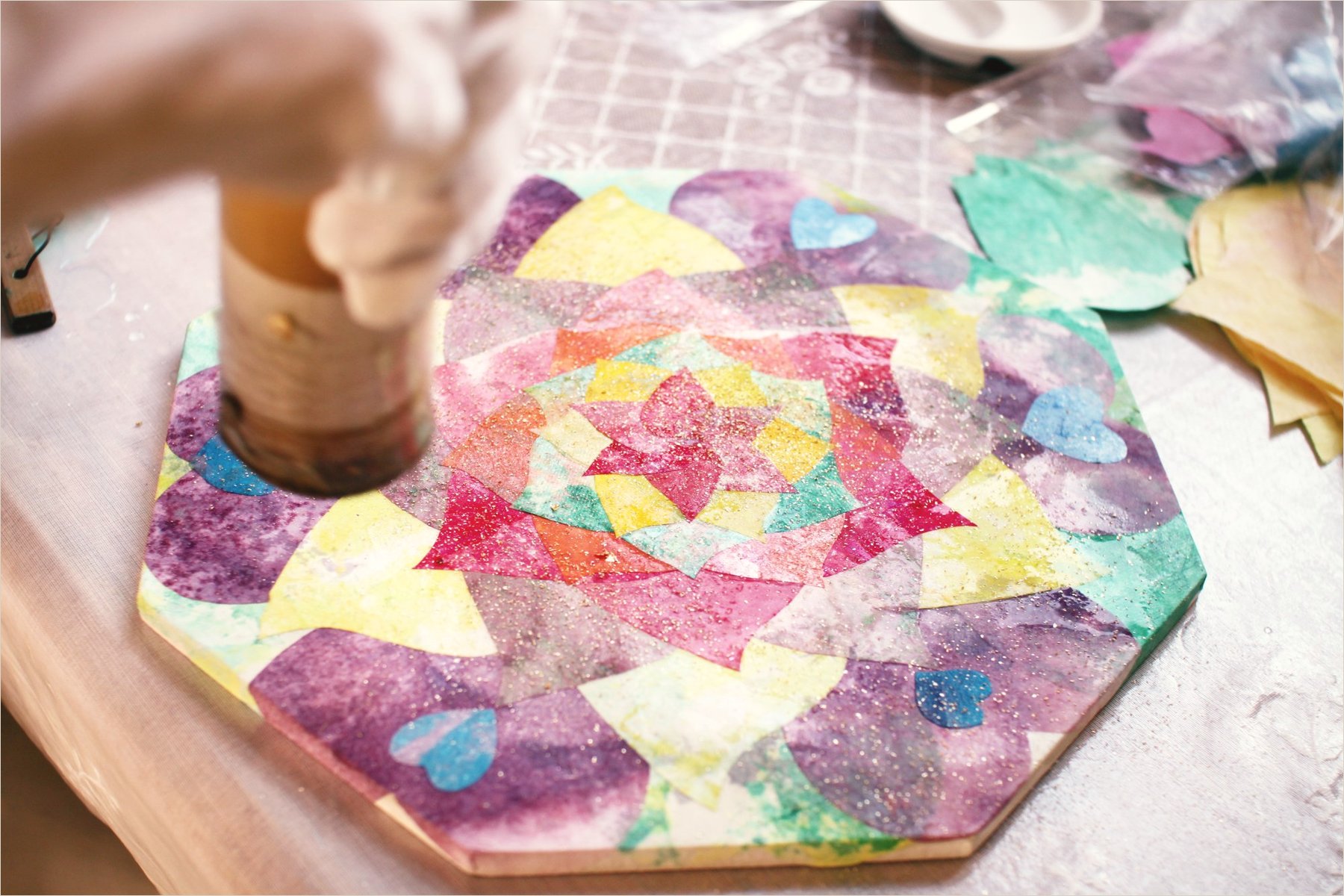 Glue-bound pigment poured from a jar onto the centre of a mandala board on the studio bench