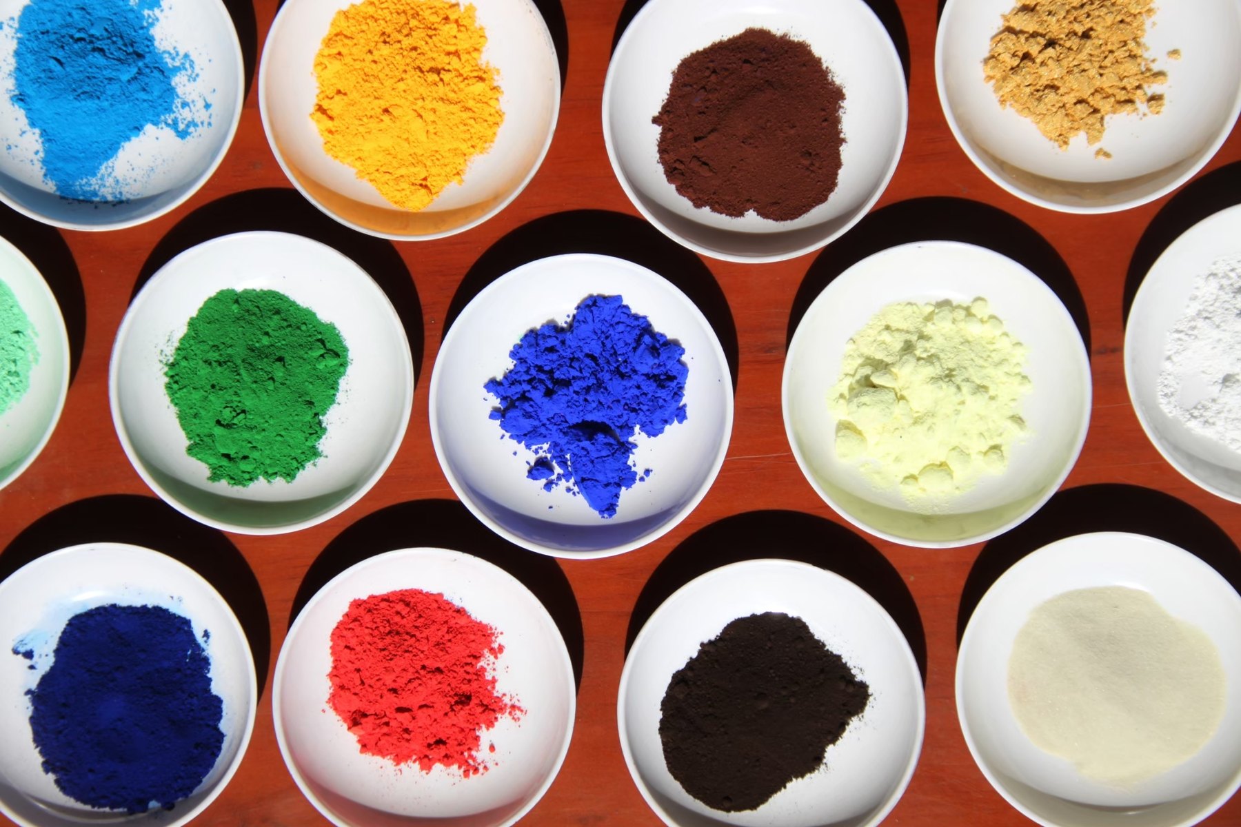 Bowls of mineral pigment, blue, green, ochre, red and black, laid out on the bench