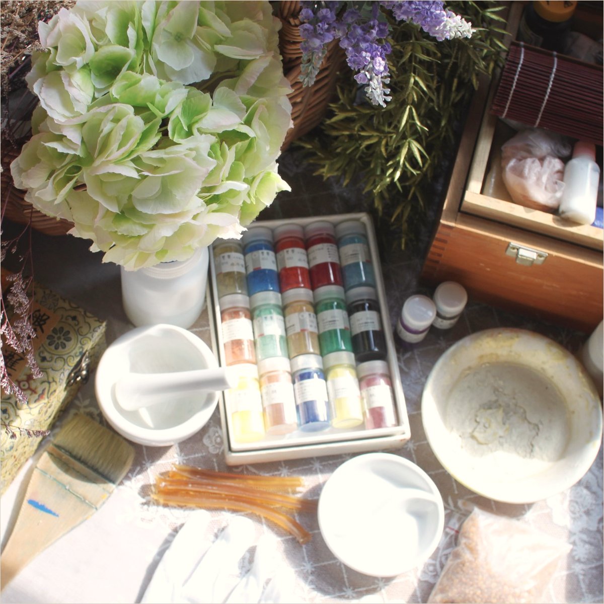 Pigment jars, a mortar, brushes and shells among dried flowers on the studio bench