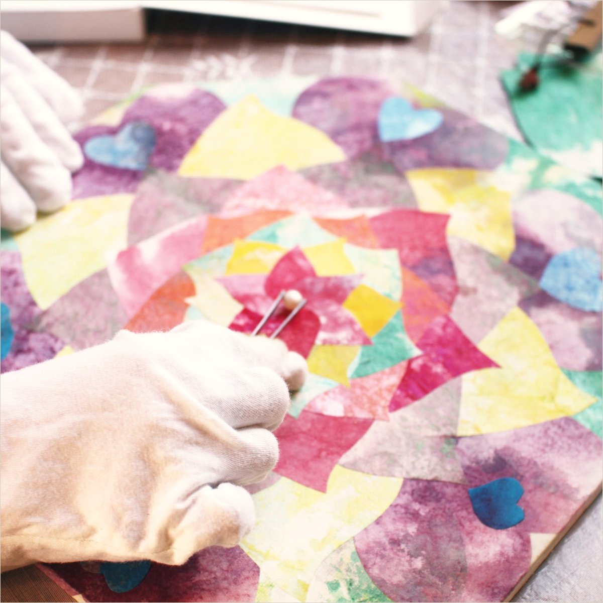 Gloved hands pressing a crystal into the crinkled petal layer of a mineral painting