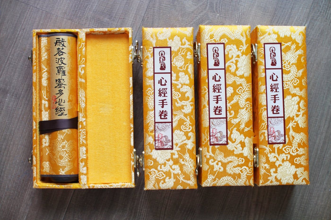 Heart Sutra handscrolls in gold brocade boxes, each labelled 心經手卷, one box open to show the rolled scroll