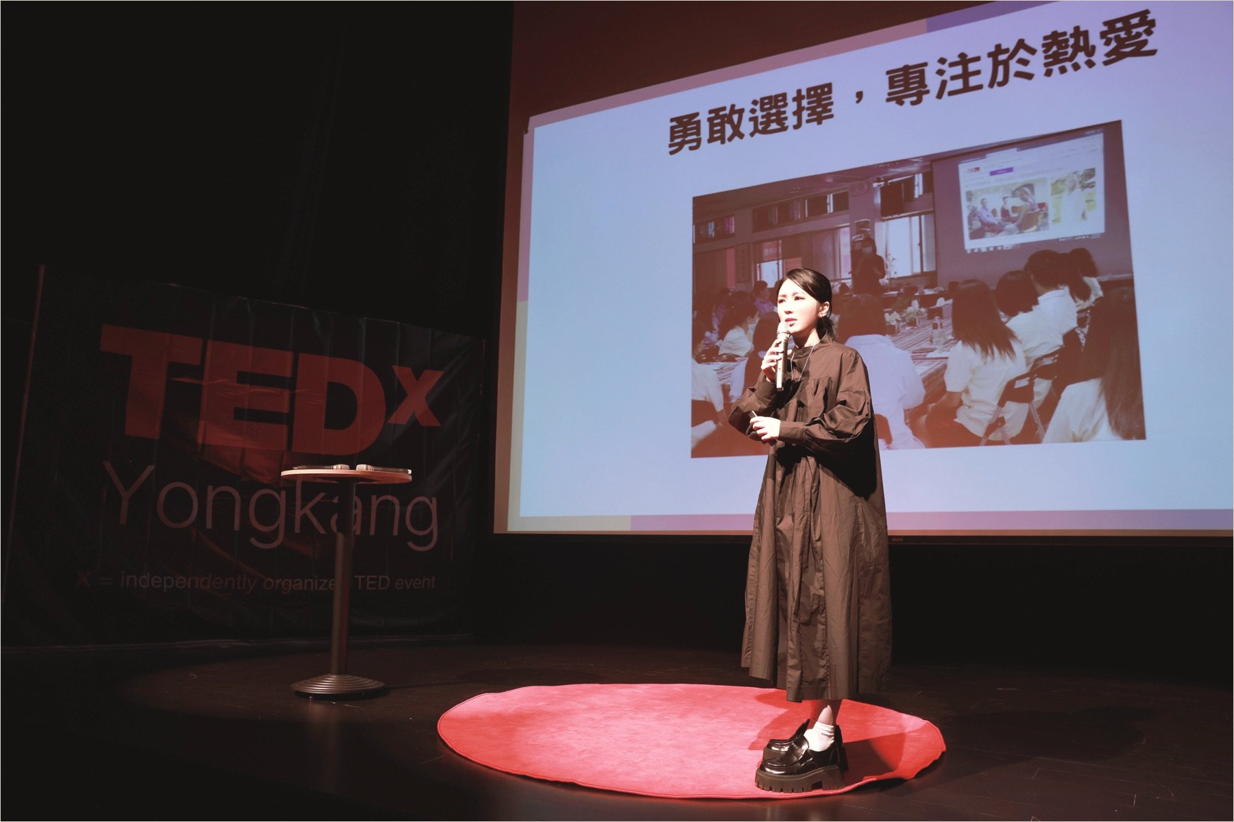 Ku Chi-Chun on the TEDxYongkang stage, the TEDx Yongkang banner at left and a slide behind her