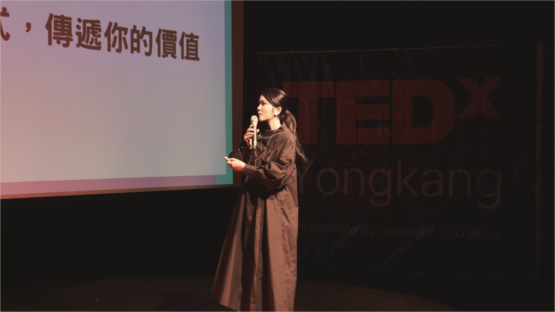 Ku Chi-Chun speaking into a microphone on the TEDxYongkang stage, the TEDx wordmark large behind her