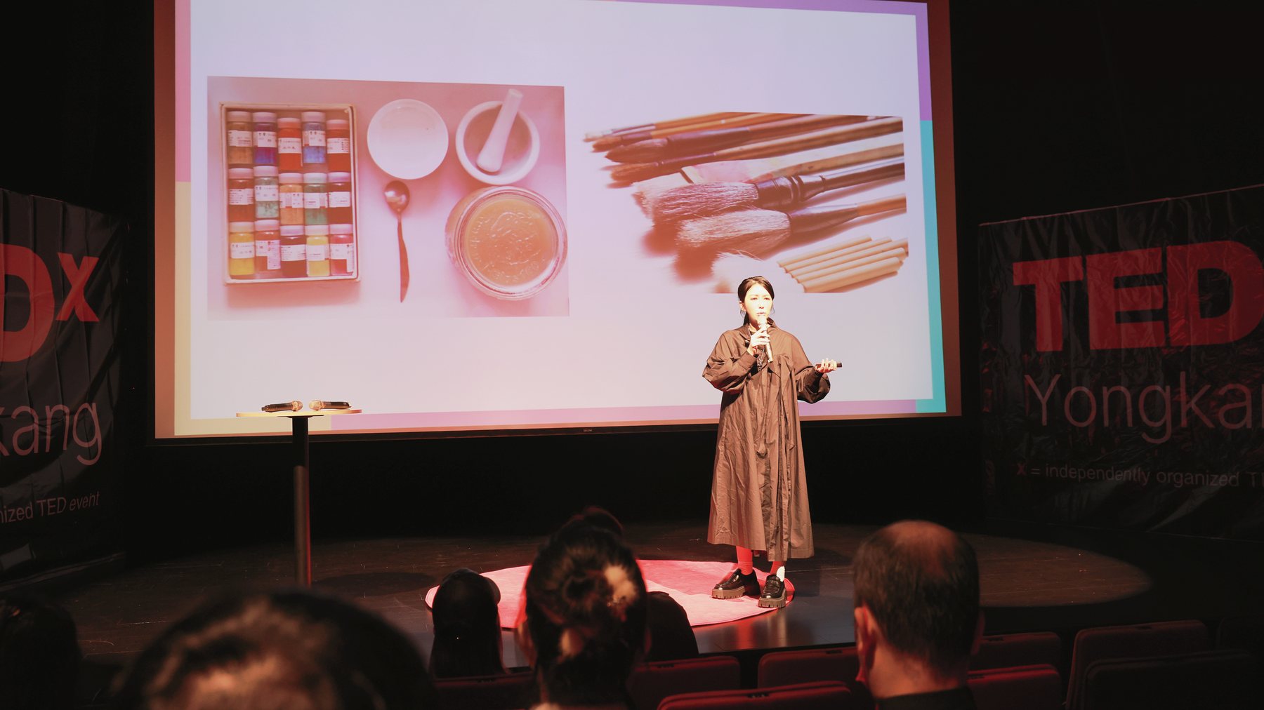 The TEDxYongkang stage: Ku Chi-Chun before a slide of her pigments, mortar, glue and brushes, the TEDx Yongkang banners at either side